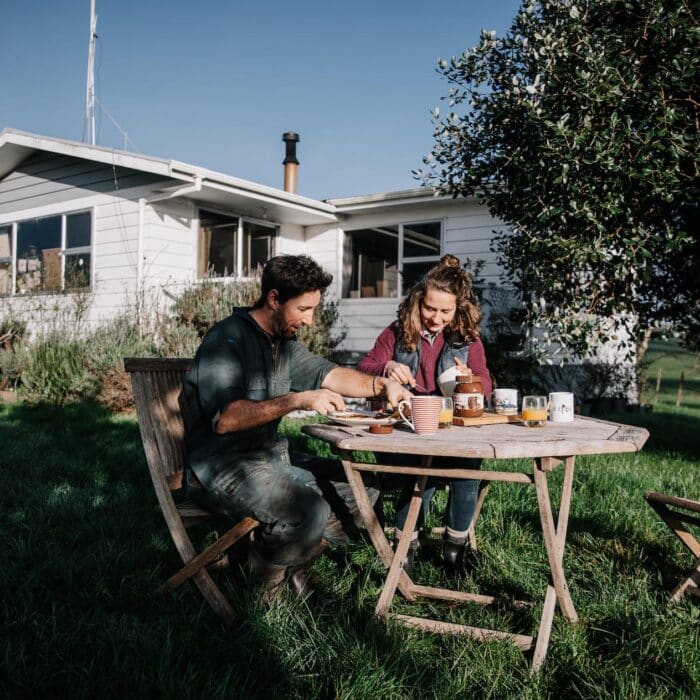 Man and woman sit at table outside their house on the farm eating pancakes.