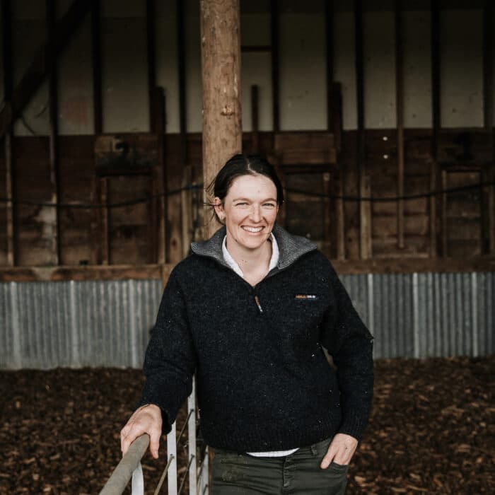 Woman leans against a fence inside a barn.