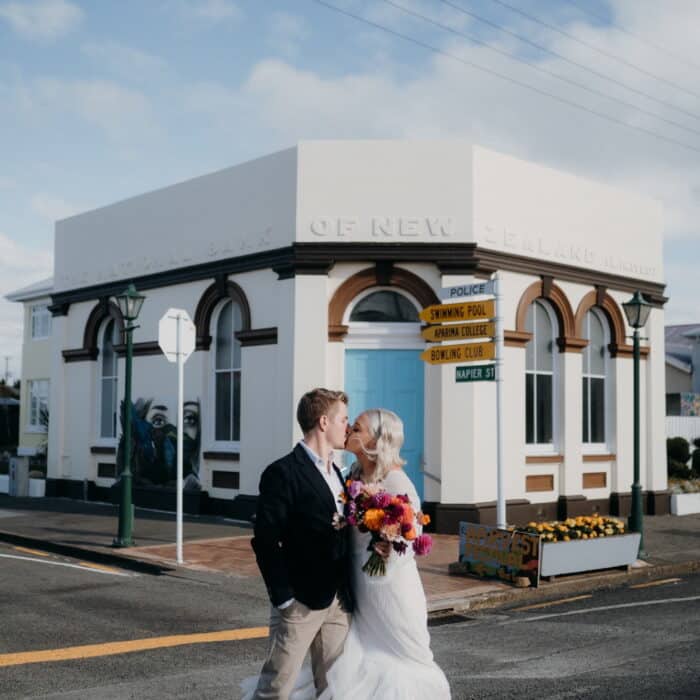 Newlywed couple kiss outside an art deco building in Aparima Riverton