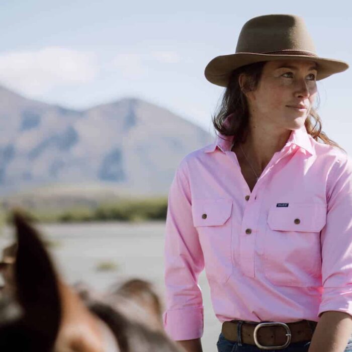 Woman in a pink shirt sits astride a horse in the high-country.