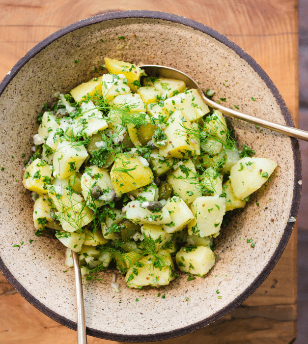 Potatoes and herbs in a salad bowl with serving spoons.