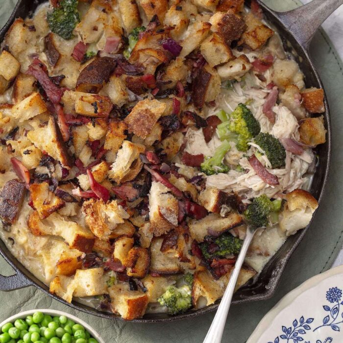 Image of a skillet of chicken casserole with a small bowl of green peas on the side