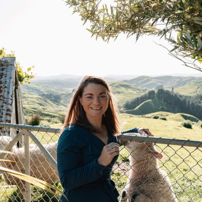 Woman leans against a farm gate and pats a sheep on the other side.